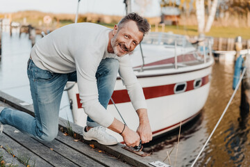 Attractive sporty man tying up the mooring rope of his yacht - obrazy, fototapety, plakaty