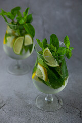 Summer mint lime refreshing cocktail mojito with rum and ice in glass on gray background. Mojito cocktail on stone table. Glassy high glass for drinks. Lemonade at the bar.