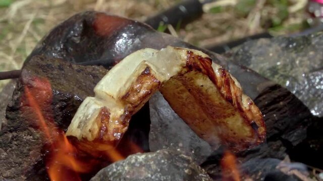 Hiker's meal. Toasting bacon and sausage on a natural fire, then dripping the fat on bread with cheese and onion on it
