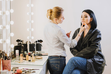 Makeup master doing makeup to beautiful model indoor beauty studio