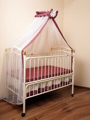 White metal four-poster bed for a newborn baby in the interior of the room. Baby cot.