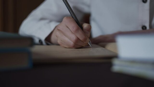 Closeup view of female hand making notes, writing letter in vintage sketchbook notebook diary. Education concept woman sits at desk, studies. Books lay on table. Keep diary of memories. Handwriting