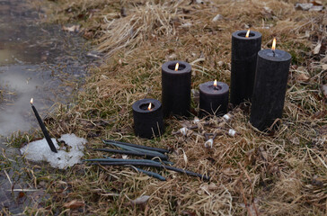 Ritual with burning black candles in the grass and snow.  Esoteric, gothic and occult background, Halloween mystic and wicca concept outdoors.