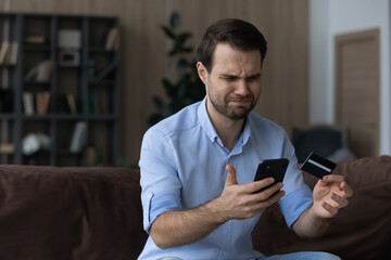 Obraz na płótnie Canvas Unhappy millennial Caucasian man frustrated by error mistake paying online on smartphone with credit card. Mad young male client or customer confused with unsuccessful internet payment on cellphone.