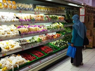 A woman is picking fruit and vegetables on a supermarket shelf