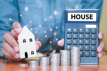 Both hands were holding a house and a calculator, and coins stacked in front of. The idea of saving money to plan to buy a house in future. Financial calculator.