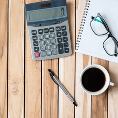 Top view Office desk with calculator, pen, eyeglasses, blank notebook and coffee cup on wood table background. workspace or home office with copy space for text concept
