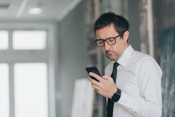 Serious businessman reading text message on smart phone