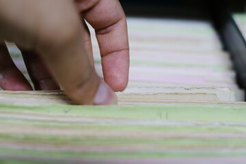 A closeup picture of a nurse's hand picking a paper medical record of a patient from a filing...