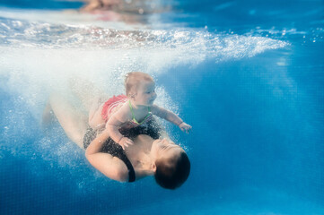 Mother holds baby, daughter learn to swim on swimming lesson, doing physical exercises, dive...