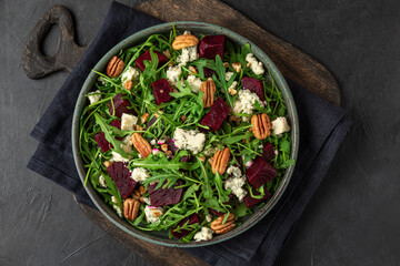 Beet or beetroot salad with fresh arugula, blue cheese and pecan nuts in a plate on black background. top view