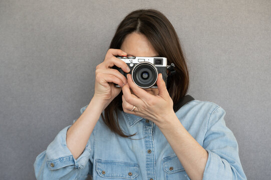 Front view of fashionable nice girl taking a picture with retro camera ,isolated on grey background