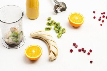 Chopped banana and two halves of orange. Cranberries and kiwi on table.