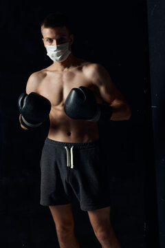 sporty man in medical mask and in boxing gloves on black background shorts fitness model
