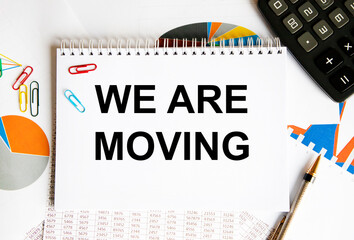 In the notebook text WE ARE MOVING, next to the pen and calculator, graphs, reports and diagrams.