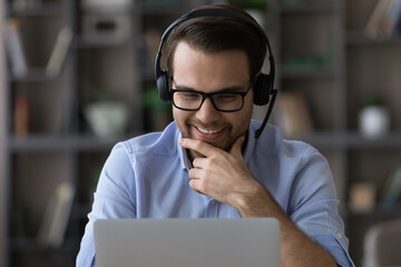 Close up of smiling young Caucasian man in headphones look at laptop screen talk speak on video...