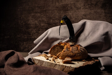Knife stuck in bread on a wooden stand on a brown background