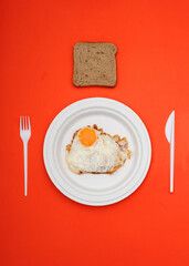 fried egg on a paper plate with plastic cutlery and toast bread on a red background.stock photo