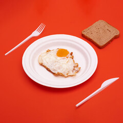 fried egg on a paper plate with plastic cutlery and toast bread on a red background.stock photo