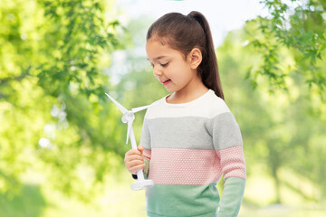 sustainable energy, power and people concept - happy smiling girl with toy wind turbine over green natural background