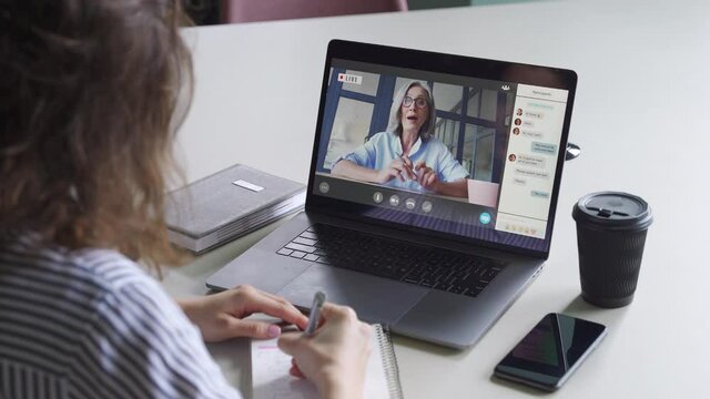 Teen girl student watching webinar, distance learning on video call with african online teacher or virtual tutor studying university seminar having online meeting on laptop screen. Over shoulder view