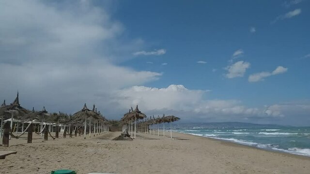Time Lapse di una spiaggia con ombrelloni e capanne di paglia su sabbia gialla, con il mare agitato, onde e nuvole veloci