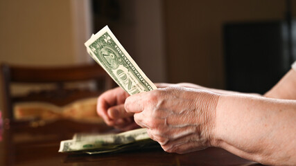 An elderly woman counts dollars. Last money for life, low incomes, poverty, 1 dollar bills.