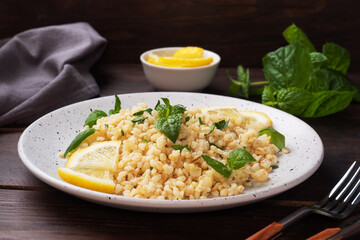 Boiled bulgur with fresh lemon and mint on a plate. A traditional oriental dish called Tabouleh. dark wooden background.