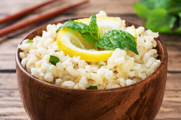 Boiled bulgur with fresh lemon and mint on a plate. A traditional oriental dish called Tabouleh. wooden background rustic