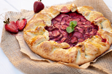 Freshly baked homemade galette or open strawberry pie and fresh mint leaves, summer food. Soft selective focus.