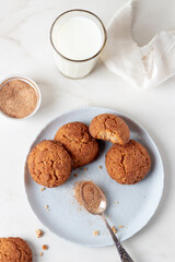 Freshly Homemade baked ginger cookies with cinnamon and sugar on gray plate and glass of milk, light marble background.