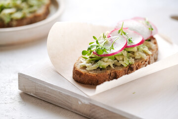 Fresh green spring sandwich with avocado and radish at light background. Copyspace