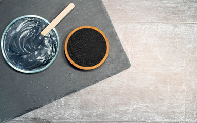 Homemade face mask and scrub with activated charcoal powder and yogurt with stick on black slate dish with jar