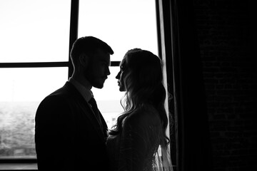 Silhouetted portrait of a bride and groom standing in front of a lacy window.