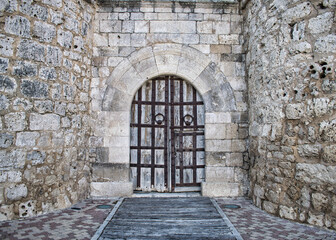 Fototapeta premium Antiguo portón de madera reforzado bajo arco de piedra en el castillo medieval del siglo XV en Portillo, provincia de Valladolid