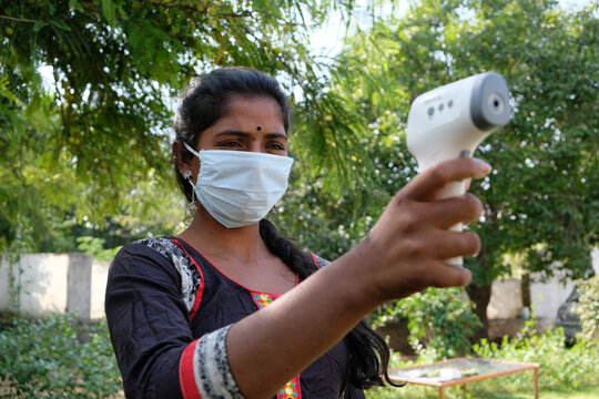 Young Indian woman wearing a medical protective face mask checking fever by a digital thermometer