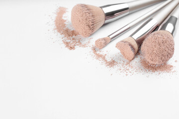Different makeup brushes with crushed cosmetic product on light background, closeup. Space for text