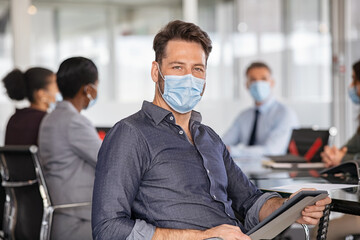 Portrait of businessman with face mask using digital tablet at office