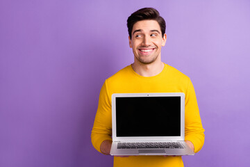 Portrait of satisfied young man hands hold laptop show display look empty space isolated on purple color background