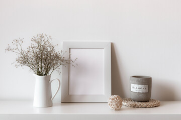 Picture frame, gypsophila flowers and scented candle on white shelf