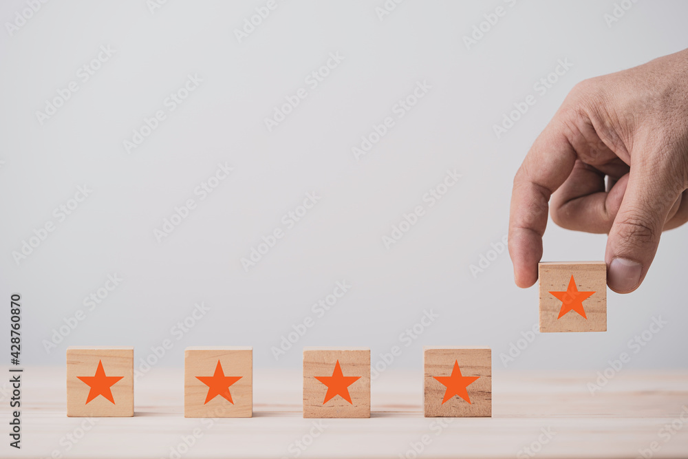 Poster Hand putting five stars which print screen on wooden cube block on table , Customer evaluation and satisfaction for product and service.