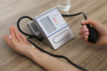 Woman checking blood pressure at wooden table indoors, closeup