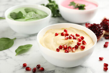 Bowl of delicious classic hummus with pomegranate seeds on white marble table