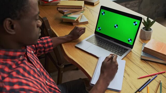 Over the shoulder black guy student with red shirt use laptop. Green chroma key screen