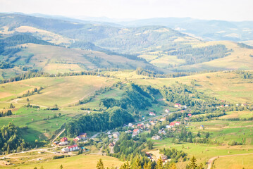 Fototapeta premium Summer landscape with village in valley and mountain in Carpathians, Ukraine. Tranquil scenery, soft focus