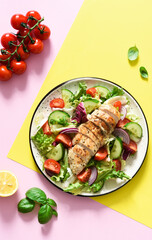 Mix of lettuce, tomatoes and grilled chicken fillet on a yellow pink background. Salad on a colored background. Food trend.