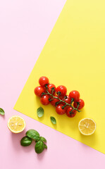 Lemon slice and bunch of cherry tomatoes on a yellow, pink background. Food trend concept.
