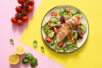 Mix of lettuce, tomatoes and grilled chicken fillet on a yellow pink background. Salad on a colored background. Food trend.