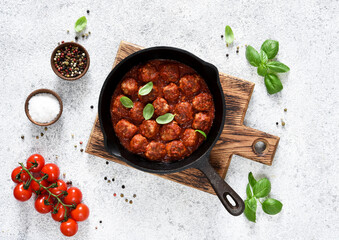Meat balls with tomato sauce in a frying pan on a light concrete background.