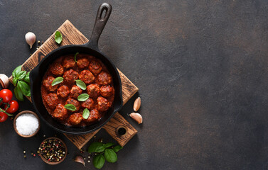 Meat balls with tomato sauce with garlic and basil in a frying pan on a brown background.